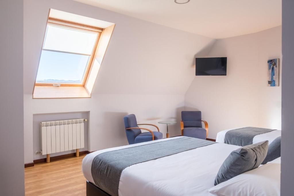 Ein Schlafzimmer mit Dachfenster, einem Bett, einem Schreibtisch, zwei Stühlen und einem Fernseher.