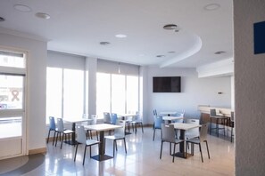 A modern dining area with tables and chairs, large windows, and a flat-screen TV on the wall. - Alda Arteixo (Abegondo)