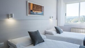 A hotel room with two beds, a window with a view, and a painting on the wall. - Alda Arteixo (Abegondo)