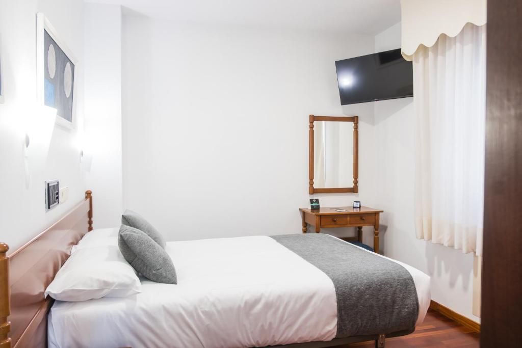 Una camera da letto con un letto, un comodino, uno specchio, una TV montata a parete e una finestra con tende.