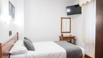 Una camera da letto con un letto, un comodino, uno specchio, una TV montata a parete e una finestra con tende.