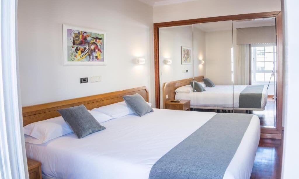 A hotel room with a bed, a nightstand, a mirror, and a painting on the wall.