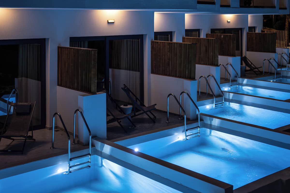 A series of indoor pools with individual changing rooms, each equipped with a shower, a towel, and a chair.