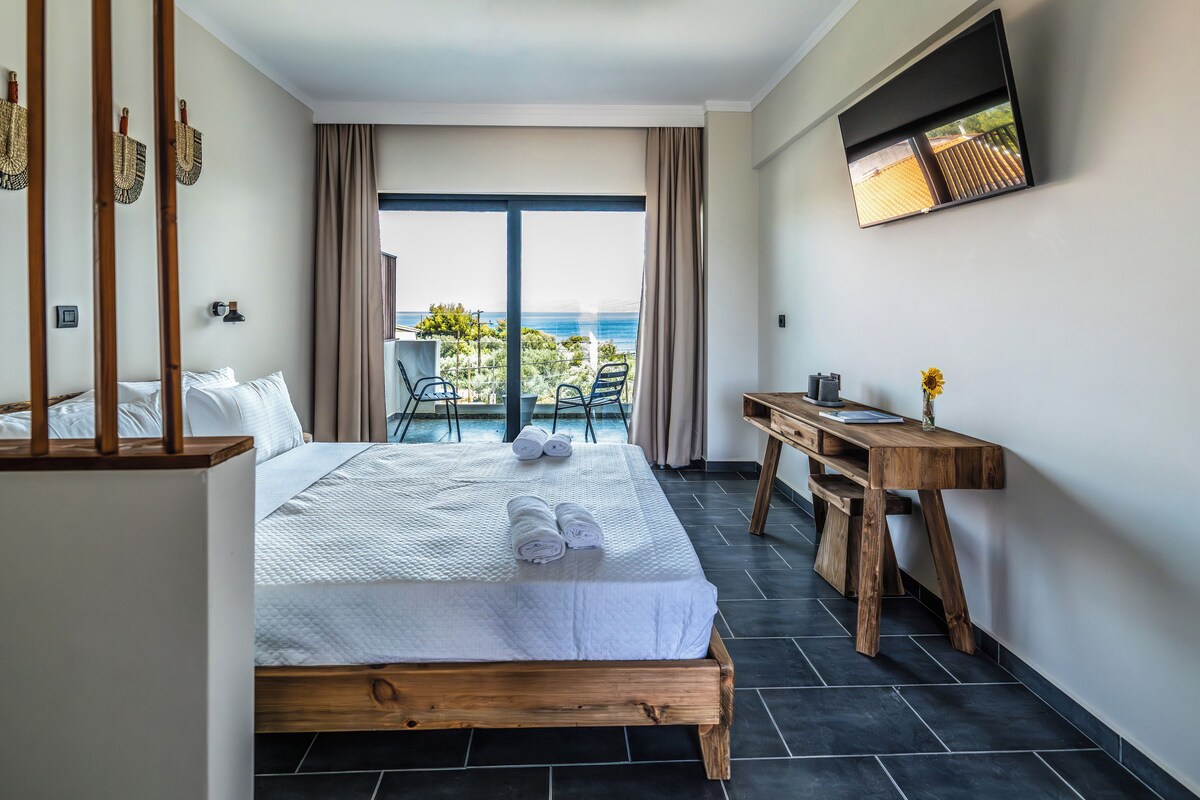 A hotel room with a large bed, a wooden desk, and a view of the ocean.