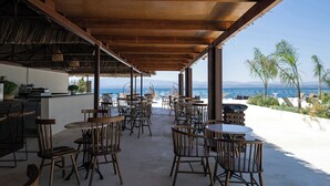 Eine Terrasse im Freien mit Holztischen und -stühlen, einer Bar und Blick auf den Ozean.