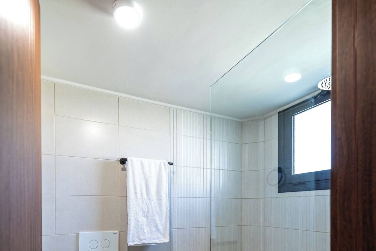 A modern bathroom with a toilet, a glass shower enclosure, and a window providing natural light.