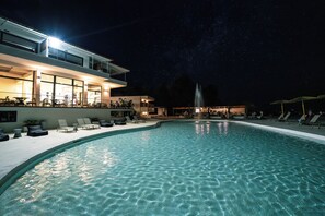 A nighttime swimming pool area with lounge chairs and a fountain. - Elion Seaside Resort (Chalcis)