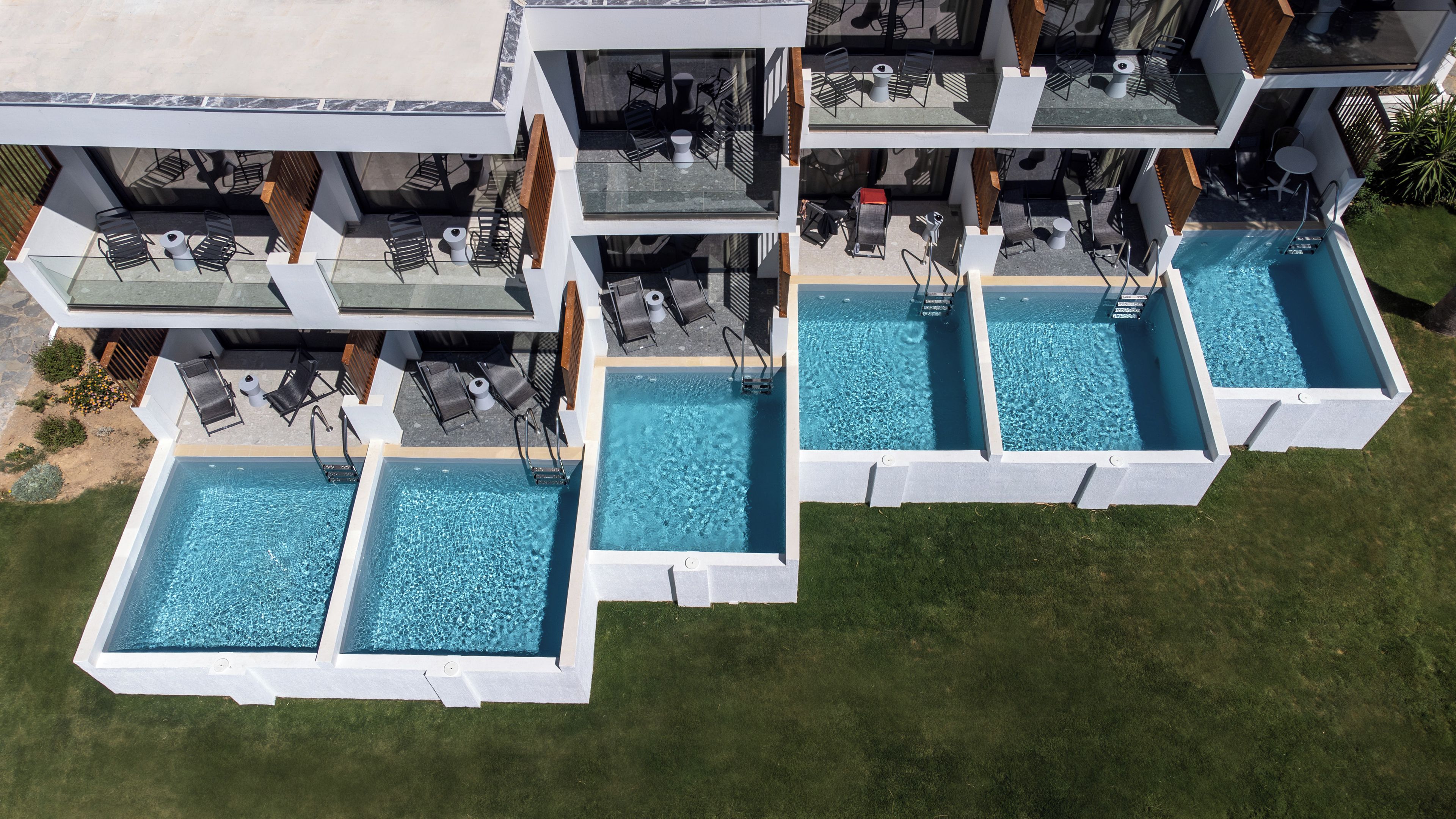 Ein modernes, mehrstöckiges Gebäude mit Poolbereich auf dem Dach, mehreren Schwimmbecken und Außen-Sitzbereichen.