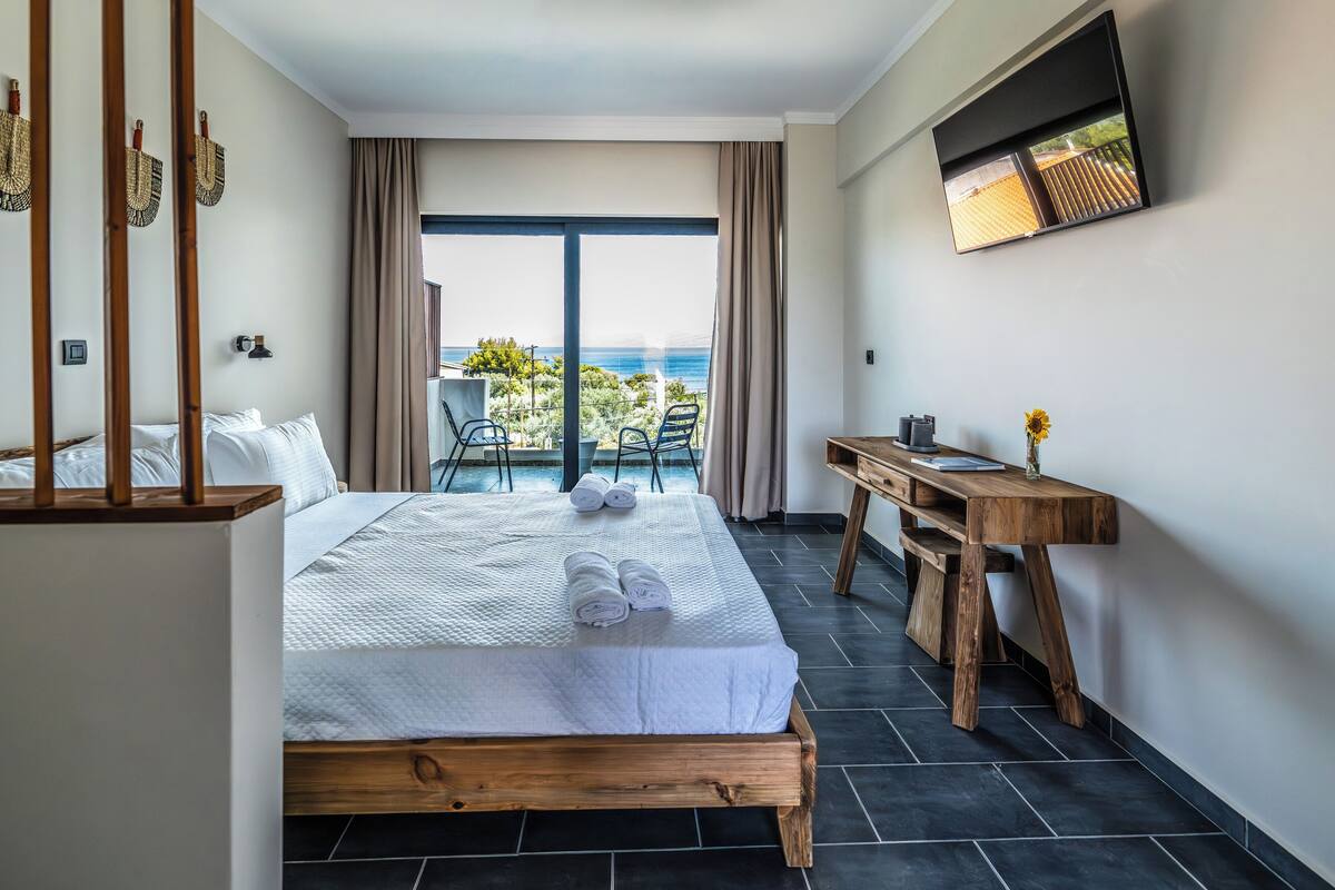 A hotel room with a large bed, a wooden desk, and a view of the ocean.