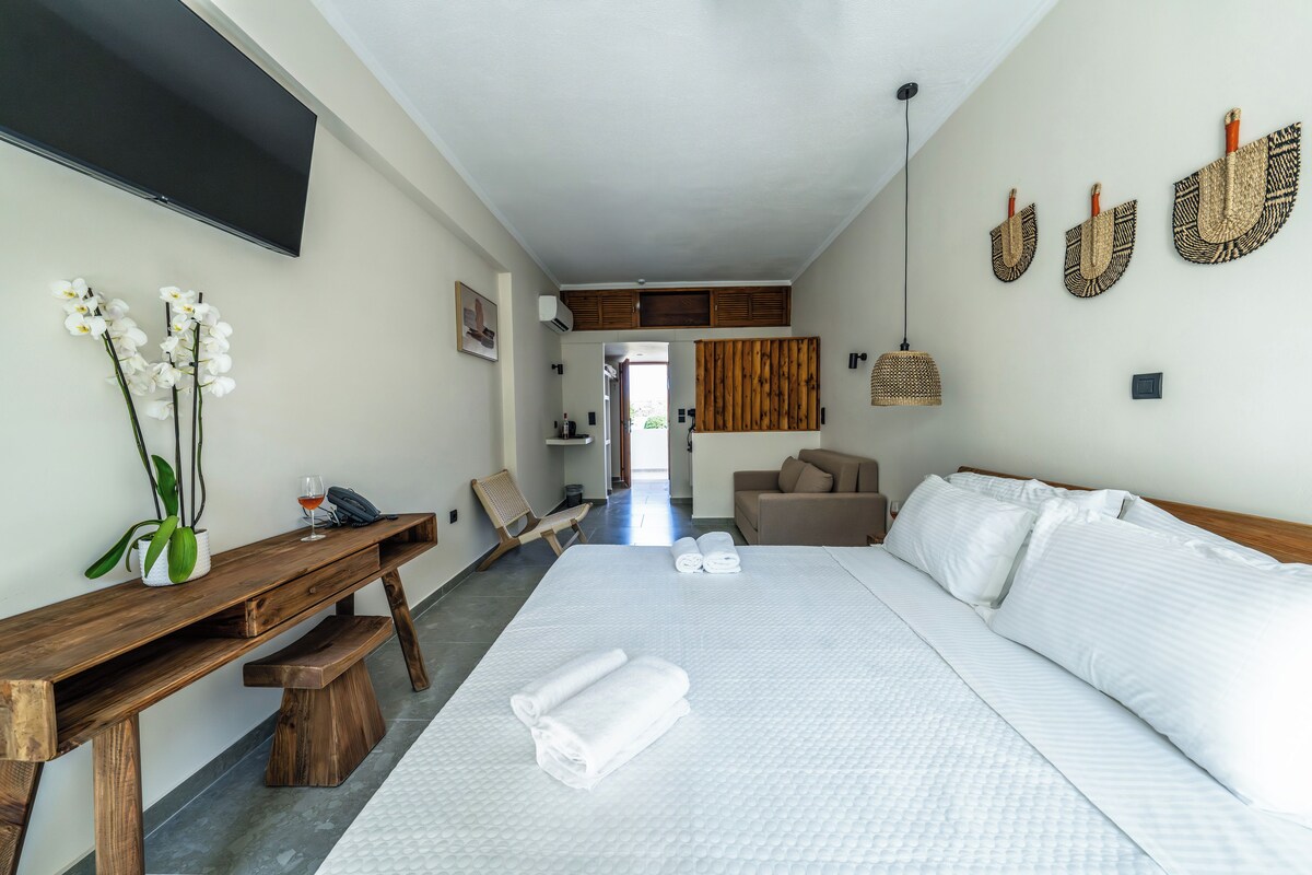 A hotel room with a large bed, a wooden bench, a desk, and a TV mounted on the wall.