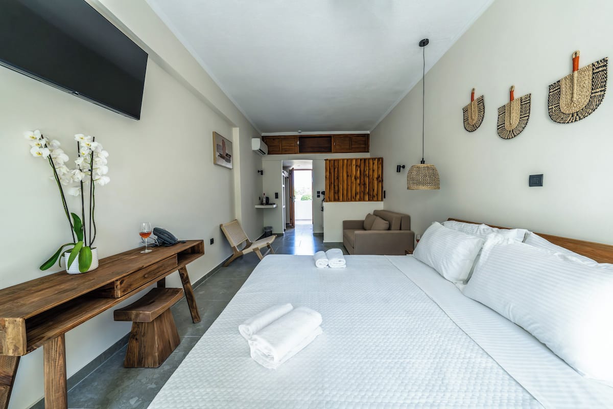 A hotel room with a large bed, a wooden bench, a desk, and a TV mounted on the wall.