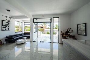 A modern living room with a black sectional sofa, a white coffee table, and a glass door leading to a balcony. - Elion Seaside Resort (Chalcis)
