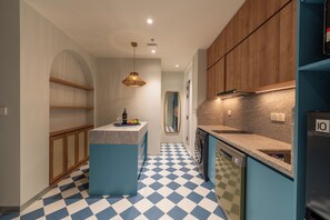 A modern kitchen with a checkered floor, wooden cabinets, a central island, and a built-in washing machine. - Solaro Hotel & Spa (Phu Quoc)