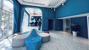 Un vestíbulo amplio con techo alto, ventanas grandes y una zona de estar central con mobiliario azul y blanco.