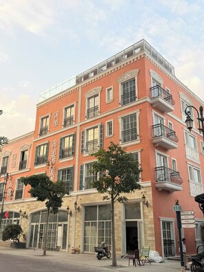 A multi-story building with a pink facade, multiple balconies, and a ground-level entrance with a glass door. - Solaro Hotel & Spa (Phu Quoc)