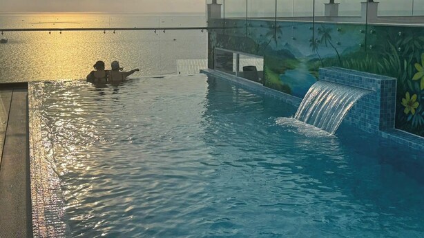 Una piscina con una cascada, barandilla de cristal y vista al mar.