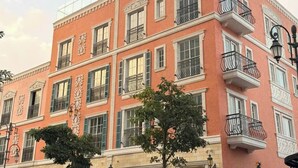 Un edificio de varios pisos con fachada rosa, múltiples balcones y entrada a nivel de calle con puerta de vidrio.