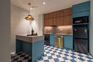 A modern kitchen with a central island, wooden cabinets, a dishwasher, and a black refrigerator. - Solaro Hotel & Spa (Phu Quoc)