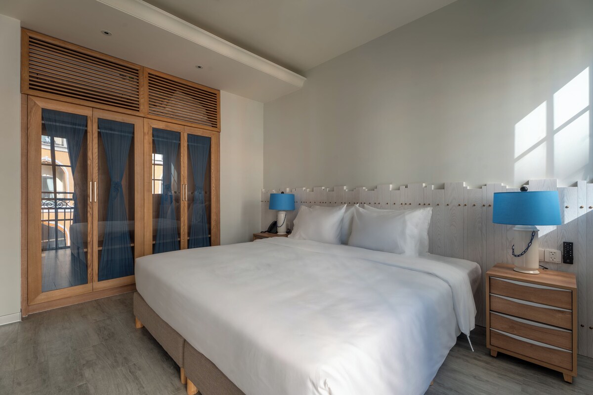 A bedroom with a large bed, wooden wardrobe, and two bedside tables with lamps.