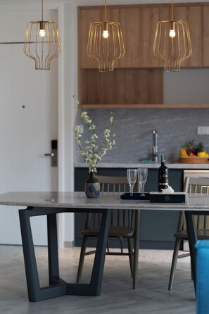 A modern kitchen with pendant lighting, a dining table, chairs, and a vase with flowers. - Solaro Hotel & Spa (Phu Quoc)