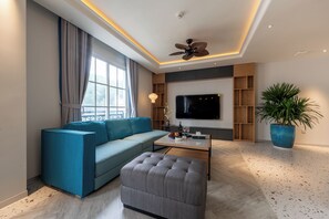 A modern living room with a sofa, ottoman, coffee table, TV, ceiling fan, and a large potted plant. - Solaro Hotel & Spa (Phu Quoc)