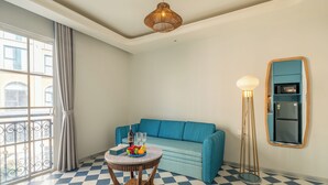 Una habitación con un sofá azul, una mesa redonda de madera con un frutero, una lámpara de pie alta y un suelo a cuadros.