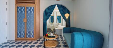 Una habitación moderna con piso a cuadros, un sofá verde azulado, un armario de madera, una mesa redonda con una bandeja y una lámpara colgante.