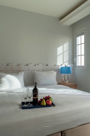 A neatly made bed with a tray of fruit and a bottle, a bedside lamp, and a window with daylight. - Solaro Hotel & Spa (Phu Quoc)