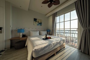 A hotel room with a large bed, bedside lamps, a painting, and a balcony with a view. - Solaro Hotel & Spa (Phu Quoc)