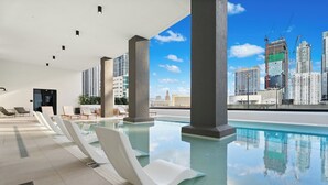 Ein Infinity-Pool auf dem Dach mit weißen Liegestühlen, großen Säulen und Blick auf die Stadtlandschaft.