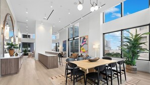 Eine moderne Küche mit einer zentralen Kochinsel, einem Essbereich mit Holztisch und schwarzen Stühlen sowie großen Fenstern mit Blick auf die Stadt.