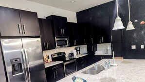 Une cuisine moderne avec des meubles de couleur sombre, des appareils en acier inoxydable, un plan de travail en marbre et un panneau décoratif sur le thème de Disney.
