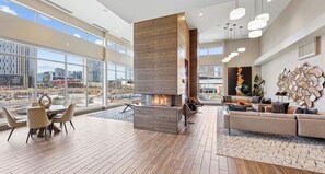 A spacious living area with a fireplace, large windows, and a view of the cityscape. - Luxury High-Rise, Walk to Broadway, Pool + Sky Lounge, coffee essentials (Nashville)