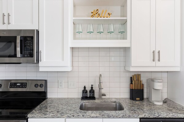 A modern kitchen with white cabinets, a stainless steel microwave, a built-in oven, a sink, and a coffee maker. - Luxury High-Rise, Walk to Broadway, Pool + Sky Lounge, coffee essentials (Nashville)