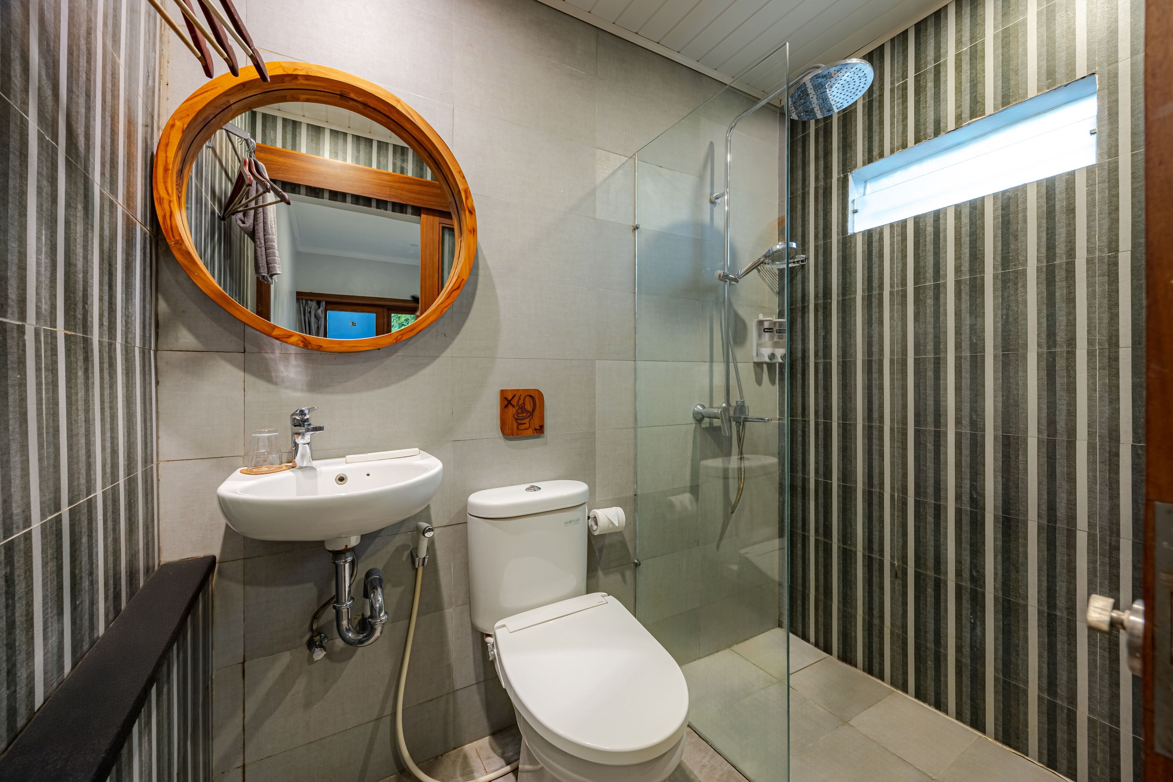 A modern bathroom with a round mirror, a sink, toilet, and a glass-enclosed shower.