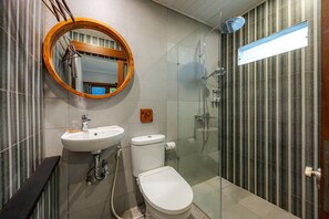 A modern bathroom with a round mirror, a sink, toilet, and a glass-enclosed shower. - Cove Ayuna (Tibubeneng)