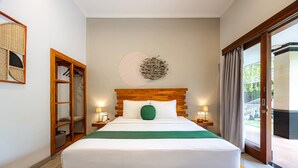 Un letto ben rifatto con una testiera in legno, un cuscino verde e una coperta bianca. Su ciascun lato del letto, un comodino in legno con una lampada. Sopra il letto, una decorazione a parete grande e rotonda.