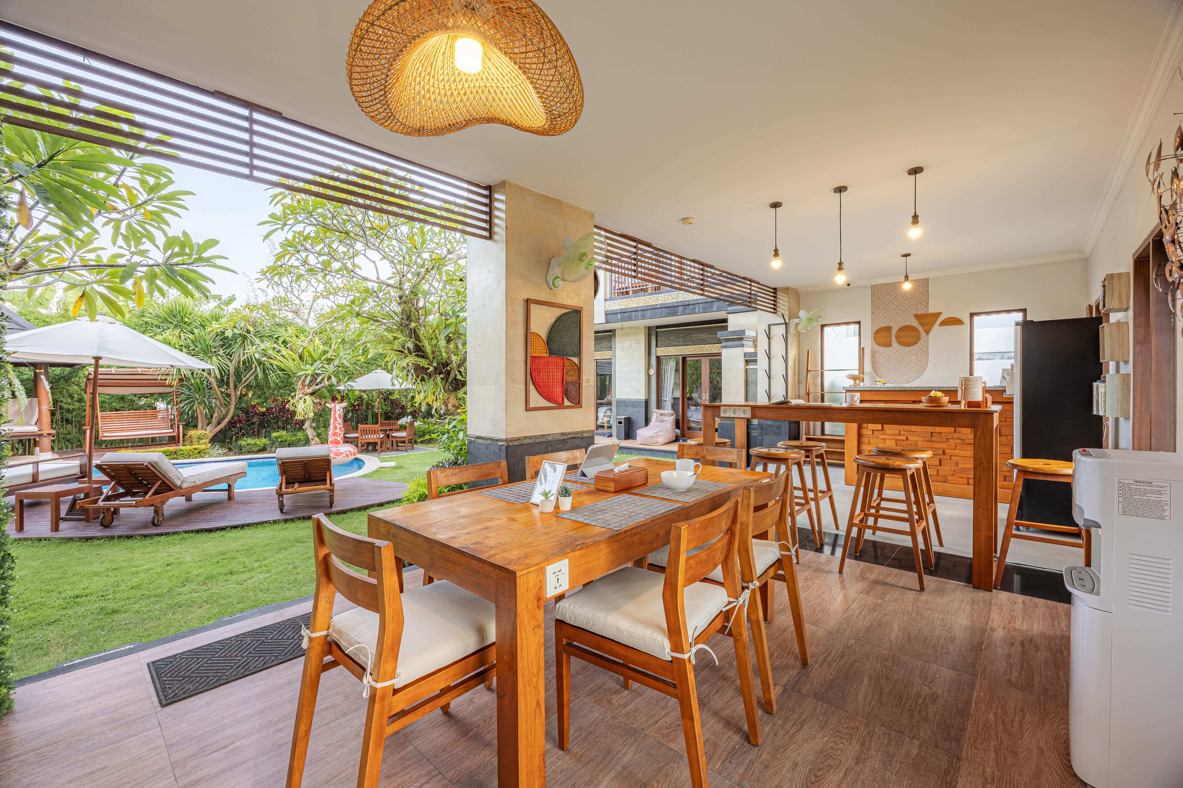 Cozinha moderna com ilha central, espaço de jantar com mobiliário de madeira e área da piscina com espreguiçadeiras e guarda-sóis.