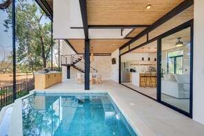 A modern indoor pool area with a wooden ceiling, a kitchen with a bar, and a dining area with a staircase leading to an upper level. - Spacious 4-Bed Home with Stunning Outdoor Living (Playa Flamingo)