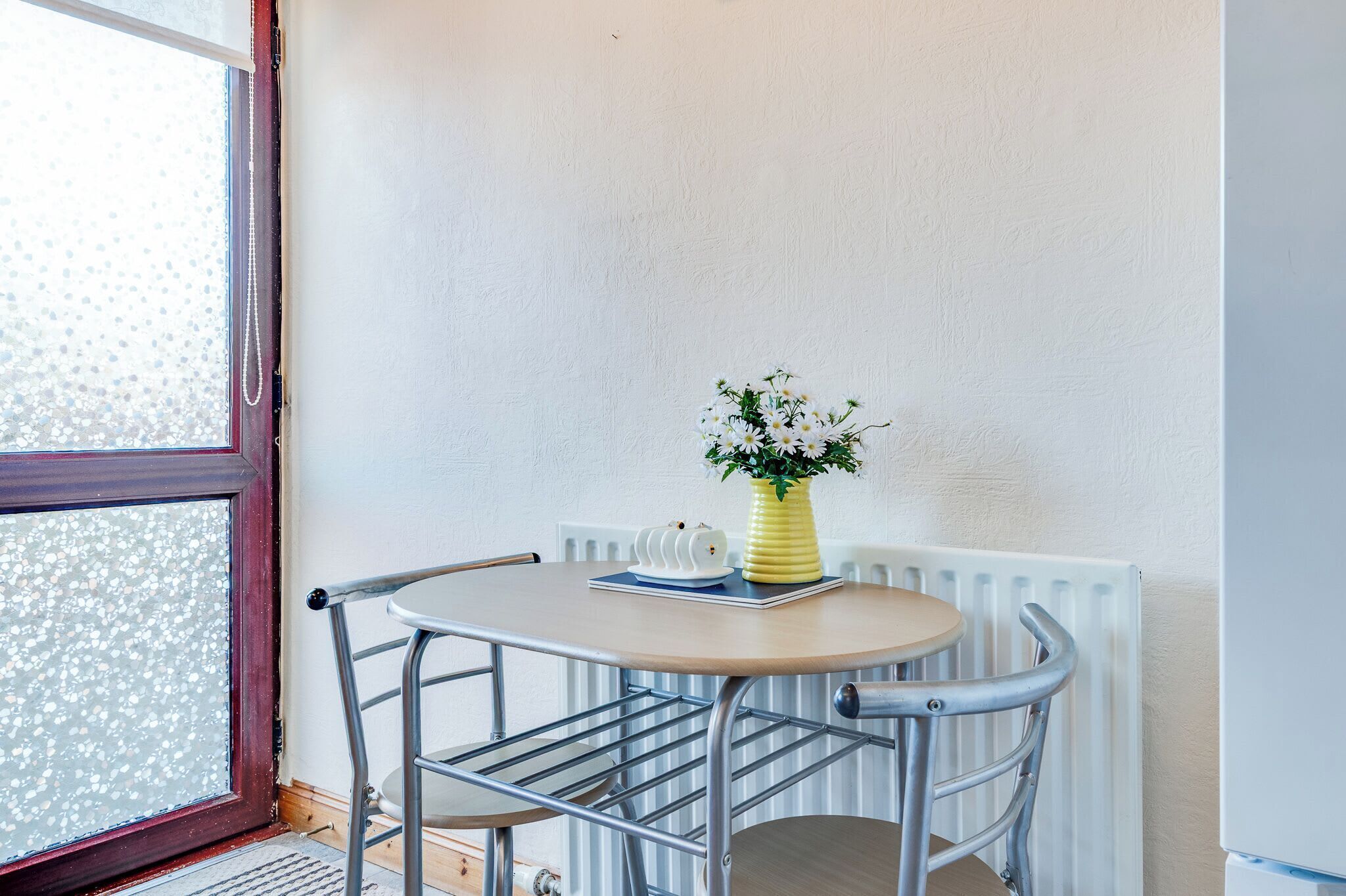 Ein kleiner runder Tisch mit einer gelben Vase voller weißer Blumen, einem weißen Tablett und einem weißen Gegenstand darauf.