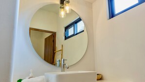 Un bany amb un mirall rodó, un lavabo blanc i una petita finestra.