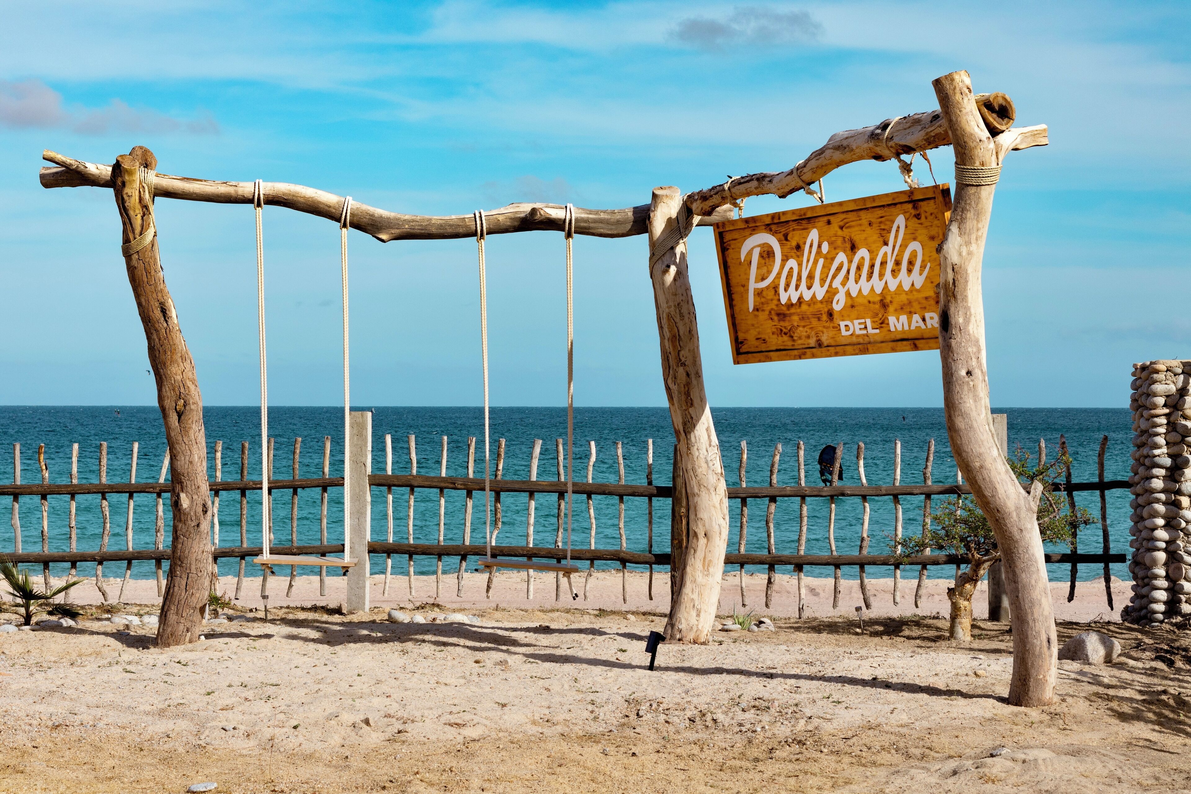 A wooden sign with the text "Polizada del Mar" and a wooden fence with a view of the sea.