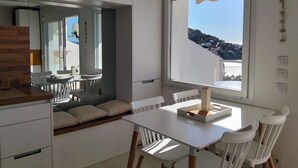 Et moderne køkken med hvide skabe, et spiseområde med bord og stole, samt et stort vindue med udsigt til en bakke.