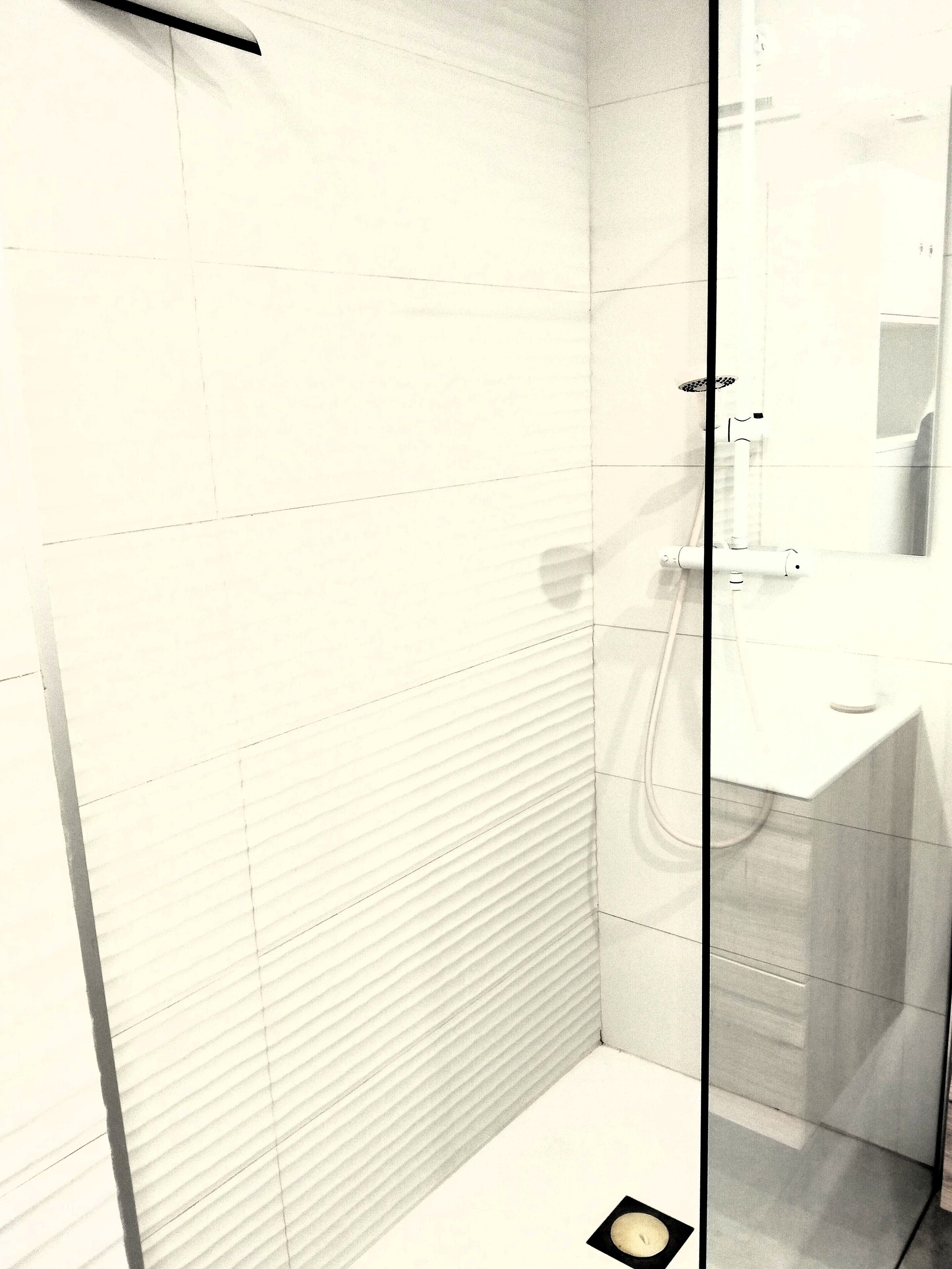 Une salle de bain moderne avec une douche à parois de verre, des murs recouverts de carreaux blancs et des toilettes apparentes.
