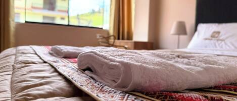 A neatly made bed with a patterned bedspread, a window with a view of buildings, and a bedside lamp.