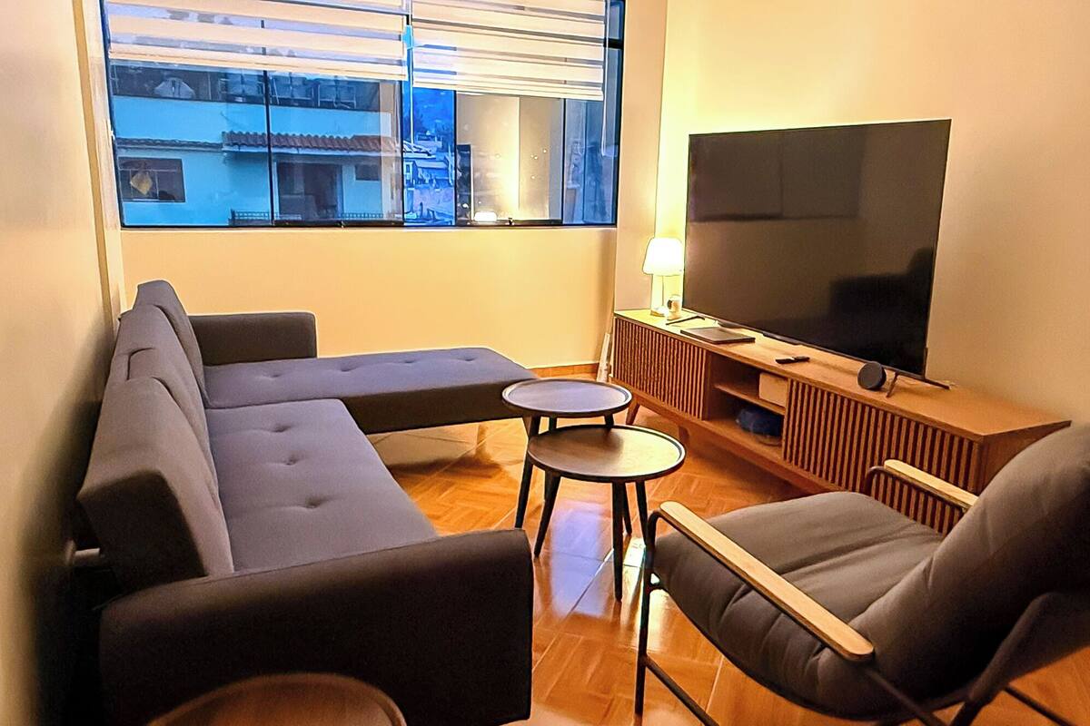 Una sala de estar con un sofá, dos sillones, una mesita y un televisor sobre un mueble de madera.