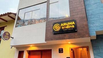 Ein mehrstöckiges Gebäude mit einem Schild für 'ARUMA andina GUEST HOUSE' und einer Treppe, die zum Eingang führt.