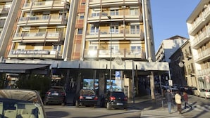 Een meerlaags gebouw met balkons, een zichtbaar bedrijfsaanduiding en een voetgangersoversteekplaats.