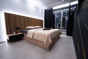 Un dormitorio moderno con cabecera de madera, cama con manta color beige, mesita de noche con un reloj y un ventanal con cortinas.