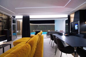 Una sala de estar moderna con un sofá amarillo, un comedor con una mesa larga y sillas, y un televisor en la pared.